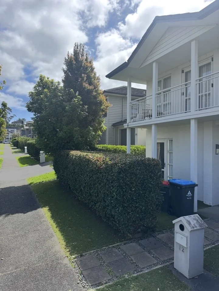 Dense trimmed hedge running along a footpath beside a white two-storey house