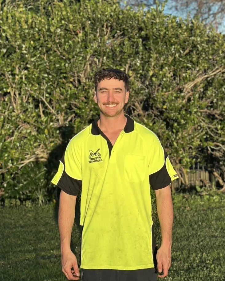 Ryan smiling in his hi-vis Trusty Trimmers work shirt in front of a hedge