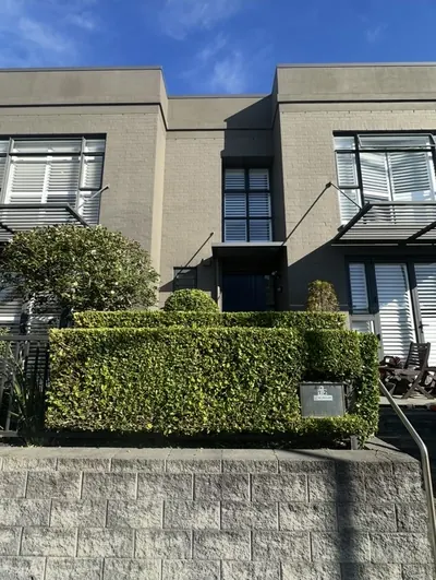 Neatly squared front hedge in front of a townhouse above a block retaining wall